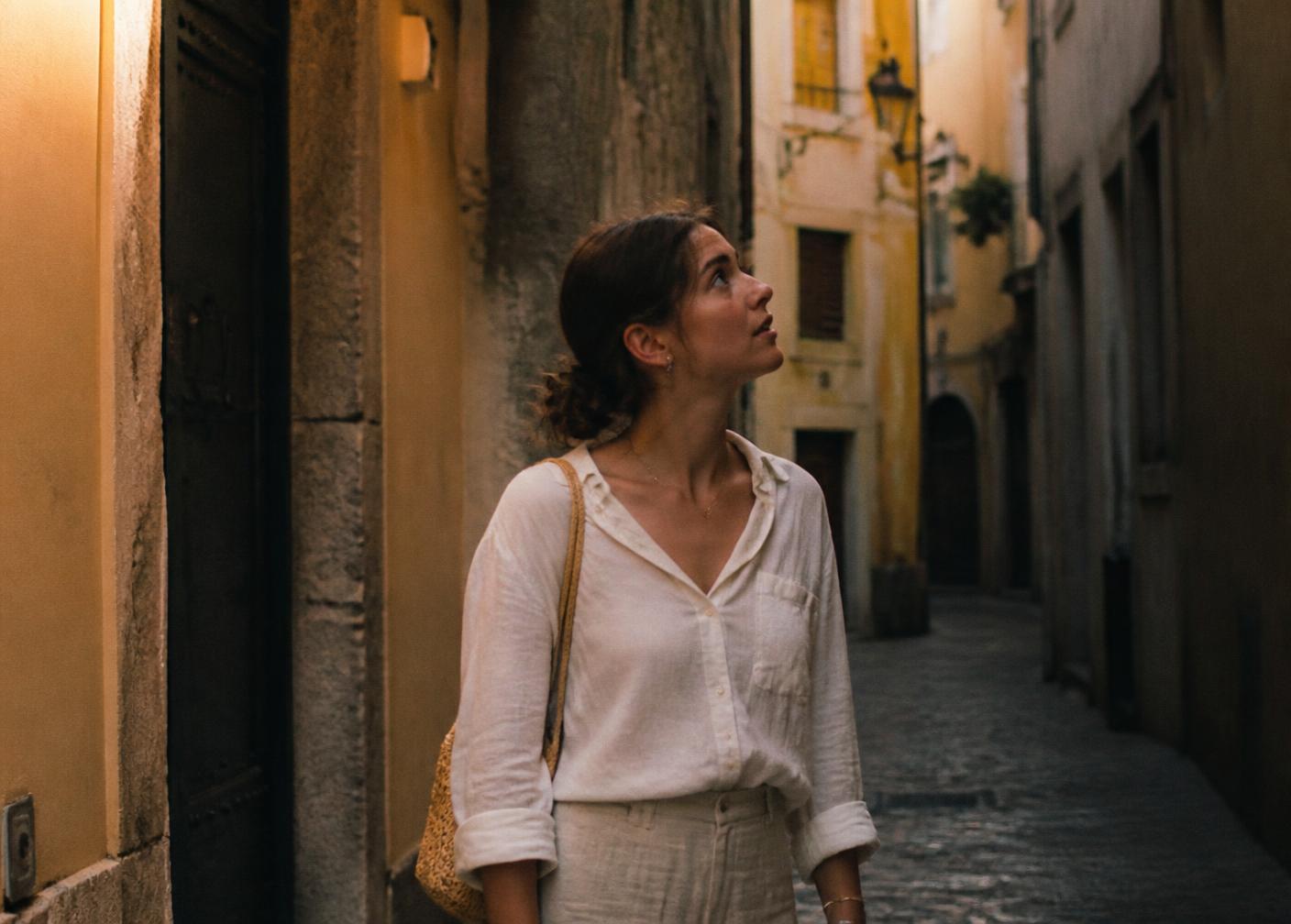 A woman pausing at an unexpected turn in a sunlit old-town alley